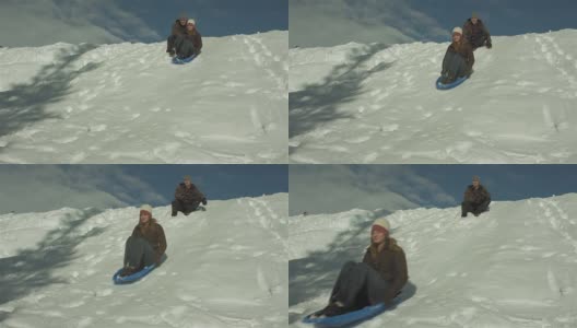 一名年轻男子推着他的女朋友坐着雪橇从雪山上滑下来。在慢动作高清在线视频素材下载