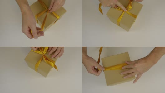 准备礼物送礼物。礼盒包装与金丝带。用手用黄丝带将礼盒包起来，打一个蝴蝶结。近上俯视图高角度。高清在线视频素材下载
