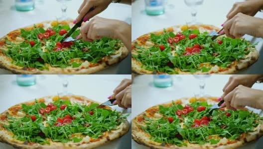 特写，大而多汁的热披萨，配上绿色蔬菜，芝麻菜和樱桃番茄。女性用刀叉切披萨高清在线视频素材下载