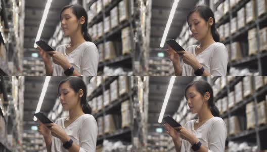 一个亚洲女人在仓库用她的智能手机检查用品高清在线视频素材下载