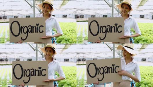 近距离观察年轻的亚洲女士农民看相机拿海报纸板与字有机靠近柜台与新鲜蔬菜。健康饮食的概念高清在线视频素材下载