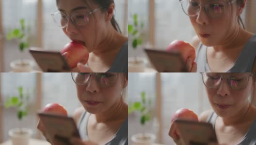 年轻健康的女性一边吃苹果一边用手机高清在线视频素材下载
