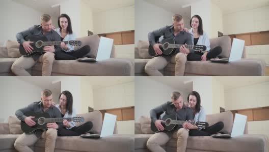 年轻夫妇坐在家里的沙发上用笔记本电脑在线学习弹吉他高清在线视频素材下载
