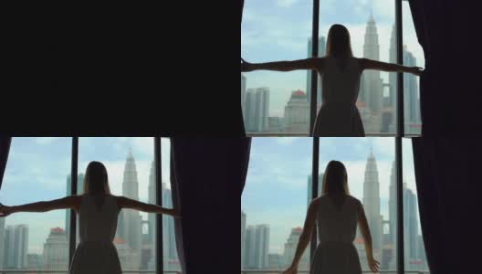 一个成功的富婆剪影拉开窗帘，俯瞰着摩天大楼林立的市中心。高清在线视频素材下载