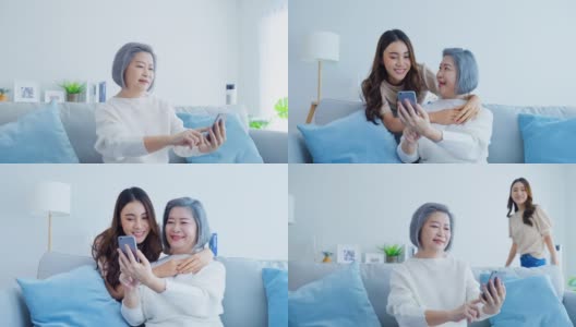亚洲幸福家庭，年长的妈妈和女儿在家里用手机。漂亮迷人的女孩惊喜的坐在沙发上，年长的母亲和网上购物聊天在客厅的房子。高清在线视频素材下载