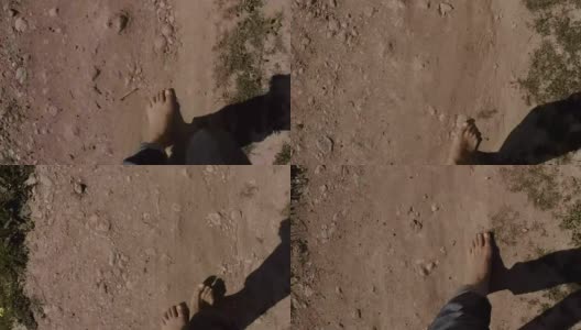 POV女士双腿不穿鞋，穿着牛仔裤走在荒芜的土地上，以第一人称视角，赤着脚，石头和沙子高清在线视频素材下载