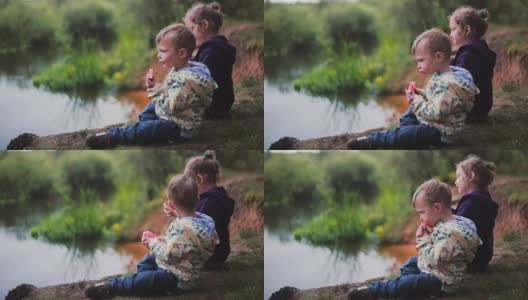侧面是两个可爱的小孩，一个男孩和一个女孩，坐在河边吃西瓜高清在线视频素材下载