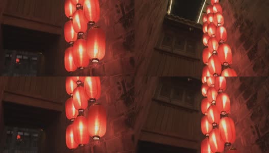 从下到上拍摄的中国寺庙的石墙和阳台在晚上。点燃的红灯笼悬挂在屋顶的柱子上，照亮灯光。传统装饰，东方节日庆典。高清在线视频素材下载