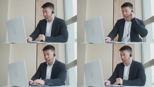 年轻的亚洲男子与耳机进行在线咨询，会议或会议使用笔记本电脑和网络摄像头的视频通话高清在线视频素材下载