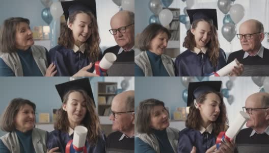 年轻的女学生穿着学位服，戴着学位帽，和父母一起在家远程学习庆祝毕业和毕业高清在线视频素材下载