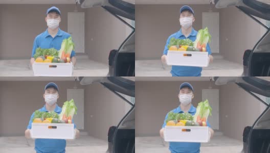 在居家隔离期间，一名亚洲快递员戴着口罩和手套，拿着装满食品、水果、蔬菜和饮料的杂货箱，站在客房前的货车旁。高清在线视频素材下载