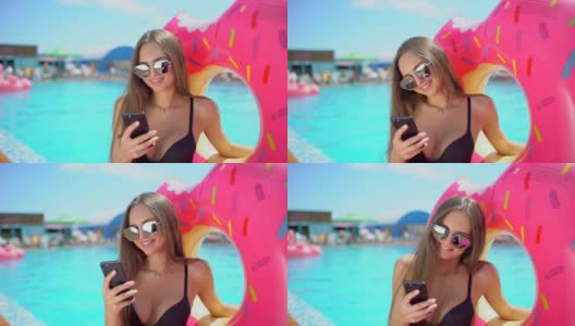 美丽的年轻女子在夏天与智能手机。比基尼女郎在泳池边打电话。女人用手机发短信，面带微笑。科技、旅游、美容、放松、慢动作的概念高清在线视频素材下载