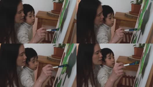 亚洲母亲有乐趣做颜色油漆与小儿子在画布上在家-母亲和孩子的爱高清在线视频素材下载
