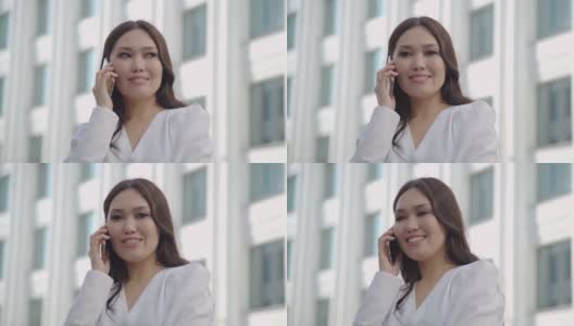微笑的亚洲女人穿着正式的西装使用手机打电话外商业手机城市智能手机。高清在线视频素材下载