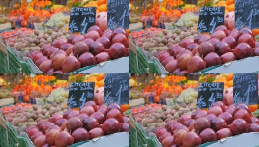 前景是大红苹果和异域水果。一个大城市的蔬菜市场。种类繁多的蔬菜和水果可供选择。健康的新鲜有机素食食品在柜台上。德语价格标签高清在线视频素材下载