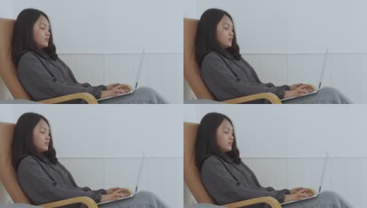 4k, Portrait，一个可爱的亚洲少女。穿着灰色衬衫坐在椅子上，带着笔记本电脑在卧室里开心地上网学习高清在线视频素材下载