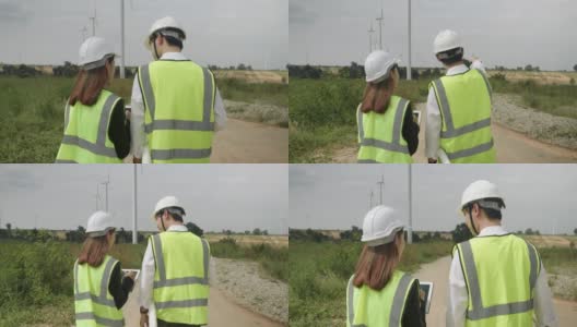 风力发电机站技术员工程师。亚洲男性工程师和女商人穿着反光夹克和头盔走在风力涡轮机农场。高清在线视频素材下载