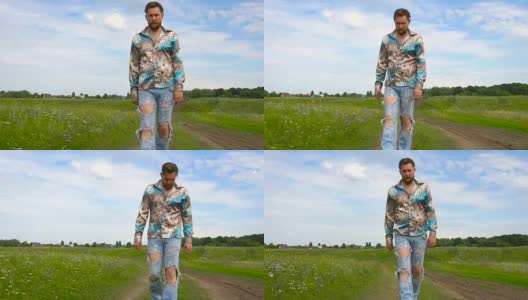 一个留着胡子，穿着破洞牛仔裤的男人在夏天沿着田野走着高清在线视频素材下载