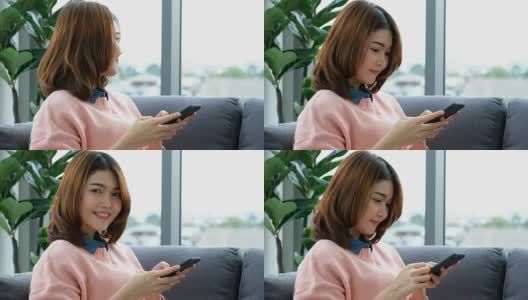 年轻美丽的亚洲女人使用智能手机与幸福，坐在沙发上与城市的看法，人们在电话，生活方式高清在线视频素材下载