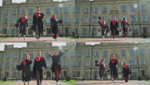 三名学生穿着黑色和红色的斗篷在大学大楼前庆祝他们的毕业。高清在线视频素材下载