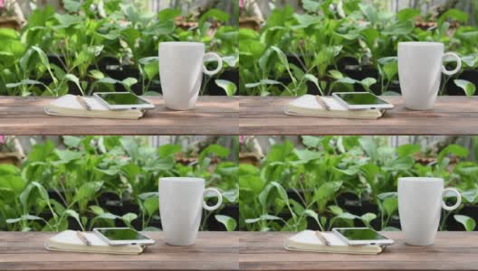 白色的咖啡杯，手机和笔记本放在绿色的户外花园的木桌上，早上的时间高清在线视频素材下载