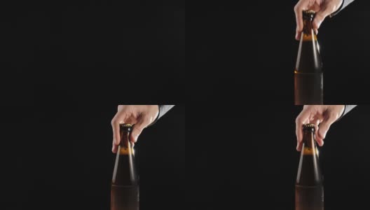 新鲜的啤酒。Hand把一个棕色的瓶子和美味的精酿啤酒放在一张黑色背景的木桌上。冰镇新鲜啤酒与水滴。准备饮料。4 k高清在线视频素材下载