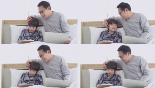 居家办公快乐的亚洲父亲使用笔记本电脑，和儿子聊天，同时做作业，坐在床上的卧室在家里。自我隔离高清在线视频素材下载
