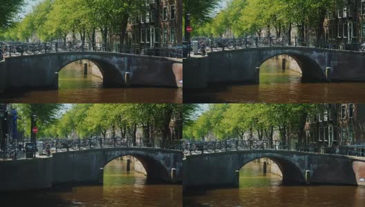 阿姆斯特丹的风景是横跨运河的桥，那里停放着许多自行车。这是一个典型的城市画面，日落前的时间高清在线视频素材下载