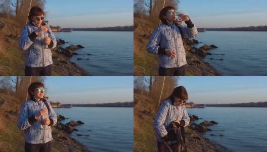 一位戴着墨镜的女游客站在秋天日落时的池塘岸边高清在线视频素材下载