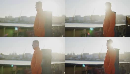 身穿橙色制服的港口工人站在船舷旁。镜头光晕。Slowmotion高清在线视频素材下载