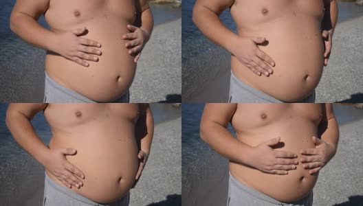 一个胖子站在海面上摸着肚子。超重与健康问题高清在线视频素材下载