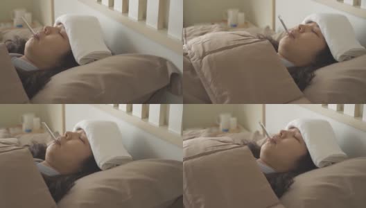 侧视图，摇摄生病的亚洲妇女躺在床上，用毛巾在额头上减轻发烧和降低体温，与口腔温度计在她的嘴里高清在线视频素材下载