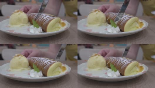 餐厅木桌上的煎饼特写。盘子里有奶油和冰淇淋。用刀切薄煎饼。高清在线视频素材下载
