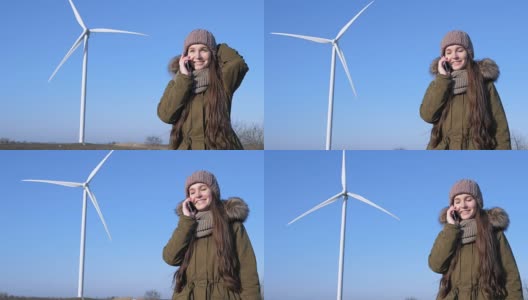 清洁能源，女孩在现代风车和天空的背景下，拿着手机微笑和讲电话高清在线视频素材下载