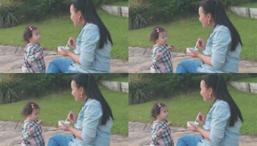 亚洲母亲在前院喂养她的混合蹒跚学步的女儿，家庭生活理念高清在线视频素材下载