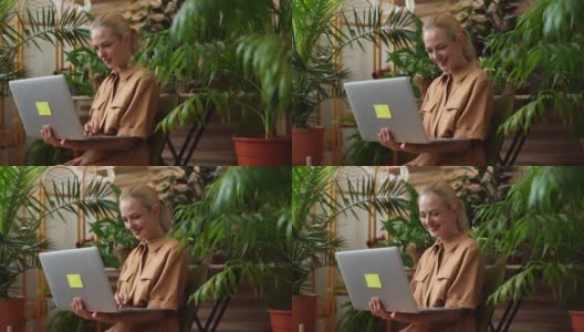 跟踪拍摄的是坐在温室里用笔记本电脑打字的大笑的女商人。高清在线视频素材下载