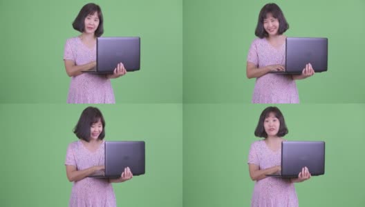 工作室拍摄美丽的亚洲孕妇使用笔记本电脑在绿色的工作室背景高清在线视频素材下载