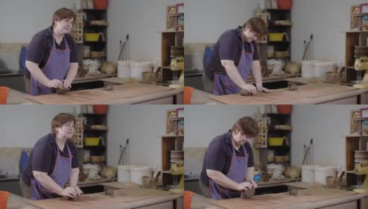 一名成年女陶工正在陶艺作坊的桌子上捣碎一块粘土，准备生产阶段高清在线视频素材下载