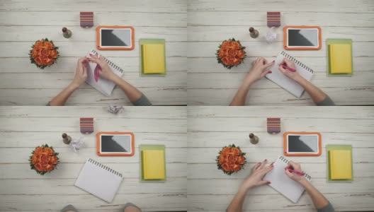 一个女孩在一张白色的木桌上写信，旁边放着鲜花和橙色的电子平板。她没有成功，他把叶子撕下来，揉成一团扔了出去。前视图。手近视图高清在线视频素材下载