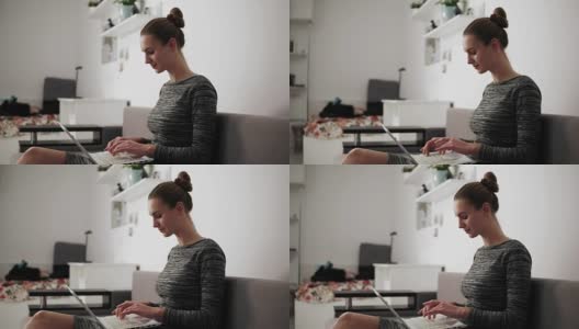 从侧面看，年轻女子坐在家里的沙发上，用笔记本电脑工作，快速地看着屏幕打字高清在线视频素材下载