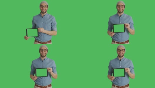 一个微笑的年轻人戴着眼镜展示绿色屏幕的平板电脑的中景。背景中的绿色屏幕。高清在线视频素材下载