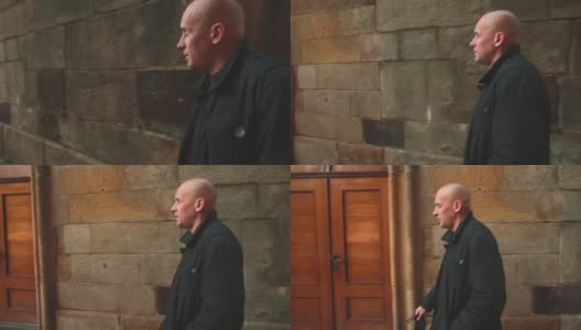 一个秃顶的男人沿着石墙走着。治疗男性型脱发的药物。高清在线视频素材下载