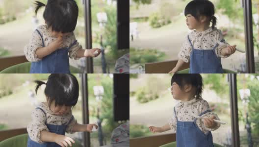 一个调皮的日本小女孩拿着叉子站在椅子上玩午餐时间，正在往嘴里吐面包。高清在线视频素材下载