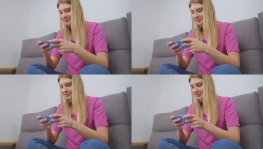 兴奋的白人女性在家里用现代智能手机玩手机游戏。快乐的年轻成年女性坐在沙发上用时髦的手机设备玩视频游戏，脸上带着愉快的微笑高清在线视频素材下载