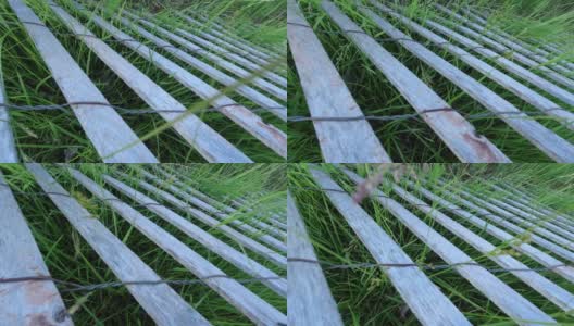 旧篱笆，木头和铁丝，用旧木板和绿草做成。乡村农场农场在村庄摄像机的视角。阳光明媚的夏天的一天。慢动作摄影小车镜头，4k。高清在线视频素材下载
