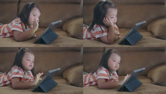 一个亚洲小女孩躺在沙发上喜欢看平板电脑高清在线视频素材下载