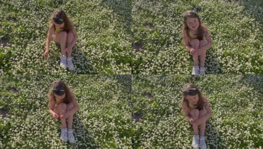 在一个阳光明媚的日子里，一个年轻的女孩在一片野花草地上采摘雏菊高清在线视频素材下载