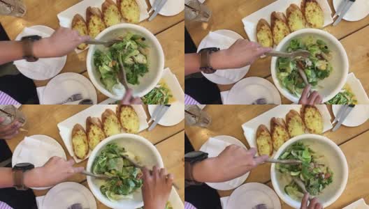 女人的手混合美味的超级食物凯撒沙拉配料与木汤匙在桌子上的餐厅大蒜面包和食物集。烹饪概念。前视图。高清在线视频素材下载