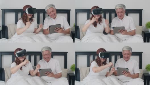 亚洲老年夫妇在家里使用平板电脑。亚洲资深的中国爷爷奶奶，在早上躺在家里卧室的床上一起玩虚拟现实游戏的概念。高清在线视频素材下载