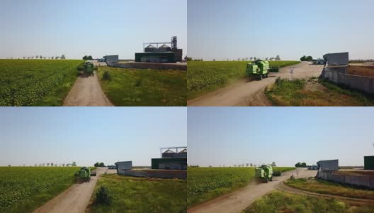 无人机摄像头跟随联合收割机行驶在向日葵种植园和谷物提升仓之间的道路上。四旋翼无人机摄像机在面粉厂或油厂附近飞行高清在线视频素材下载